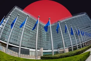 A wide-angle, slightly distorted view of the modern, curved glass facade of a European Commission building. A long row of flagpoles flying the blue and yellow European Union flag stands in the foreground. The building is set against a stark dark background dominated by a massive, solid red circle rising behind it.