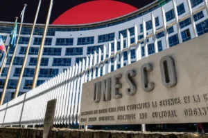 The curved, multi-story facade of the UNESCO headquarters building with a large stone sign in the foreground displaying the 'UNESCO' name. The structure is set against a stylized dark background dominated by a massive, solid red circle rising behind it.