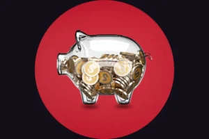A transparent glass piggy bank partially filled with gold coins bearing the dollar symbol. The piggy bank is centered against a dark background featuring a large, solid red circle directly behind it.