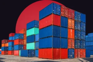 An industrial port scene featuring massive, towering stacks of colorful shipping containers in blue, red, and teal. The containers are set against a dark background with a large, solid red circle rising behind them.