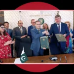 Government officials shaking hands and holding signed bilateral folders during a formal signing ceremony, set against a dark background with a red circle